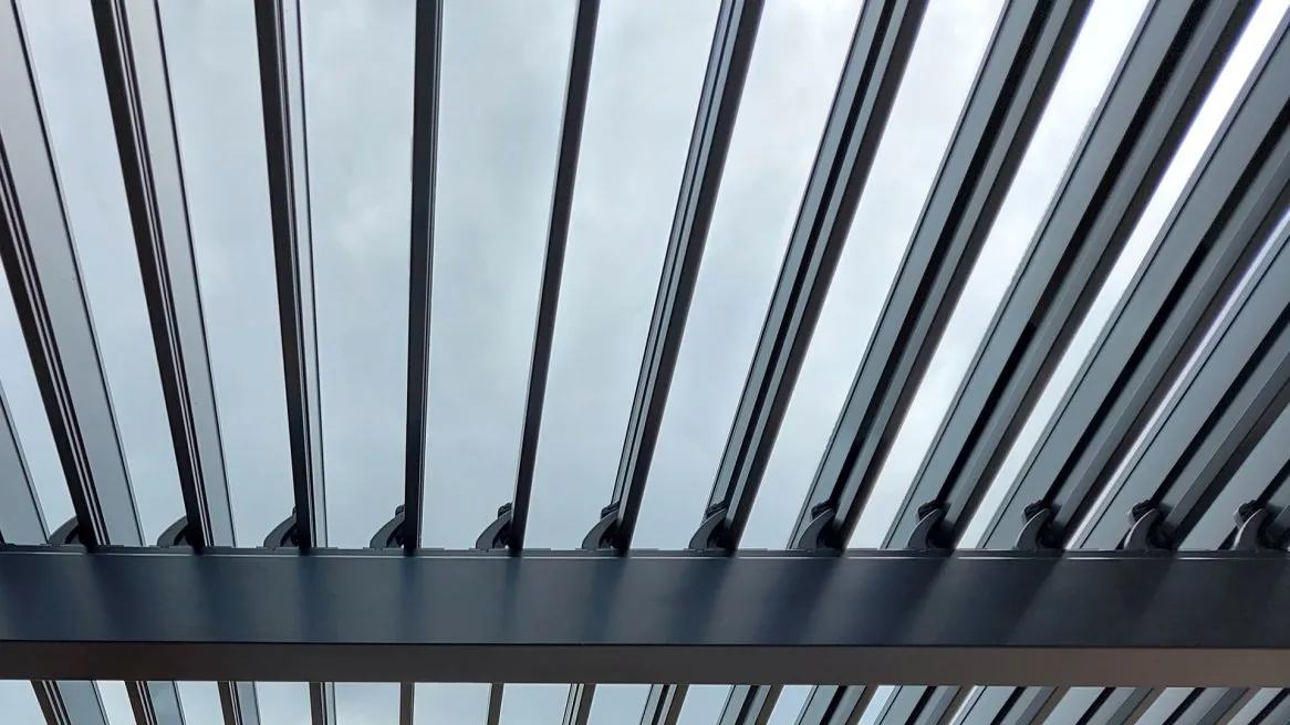 Vue en contreplongée d’une structure en métal avec des lames, laissant entrevoir un ciel nuageux.