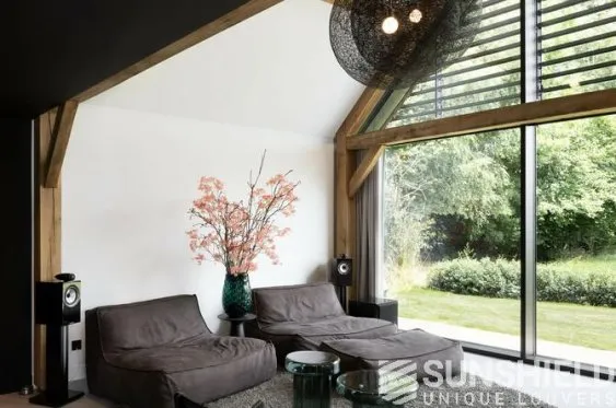 Salon moderne avec canapé confortable, vase de fleurs, plaques de bois et grandes baies vitrées sur jardin verdoyant.