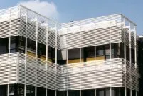 Immeuble moderne avec façades en lattes blanches, fenêtres noires et accents jaunes, le tout baigné de lumière naturelle.