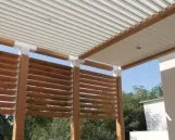 Poutres en bois et lames orientables sous un auvent, offrant une protection solaire et une belle vue sur le jardin.