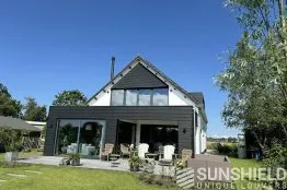 Maison moderne avec façade en bois, terrasse accueillante et jardin verdoyant sous un ciel bleu, parfaite pour la détente.