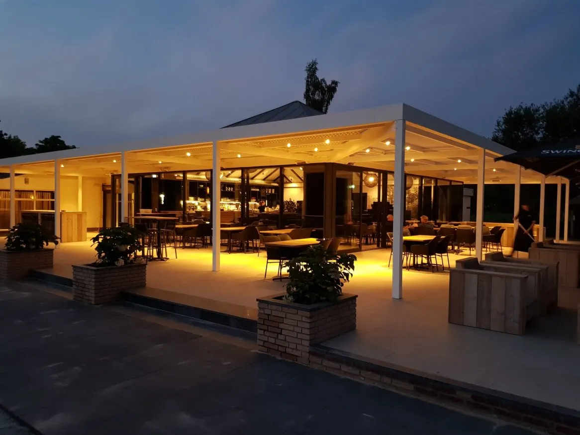 Restaurant en extérieur illuminé le soir, avec des tables et chaises sous une terrasse moderne, ambiance chaleureuse et accueillante.