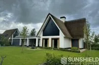 Maison moderne avec toit de chaume, jardin verdoyant et façade élégante. Parfaite harmonie entre design et nature.