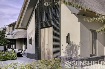 Façade moderne d’une maison avec porte en bois, volets design et jardin verdoyant, créant une ambiance accueillante.