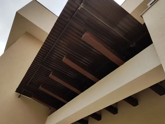 Visuel d’un auvent moderne en métal noir, surplombant un mur beige d’une construction contemporaine.