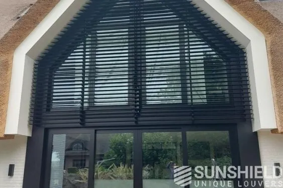 Façade élégante avec des persiennes noires et une grande porte vitrée, fusion de modernité et design architectural unique.