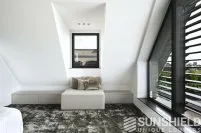 Intérieur moderne d’une chambre sous les combles, avec un grand tapis et un coin détente confortable près d’une fenêtre.
