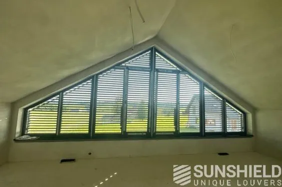 Fenêtre moderne en triangle avec lames orientables, offrant une vue sur un paysage verdoyant à l’extérieur.