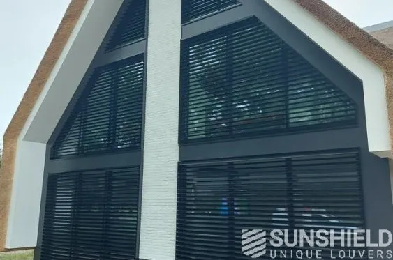 Façade moderne d’une maison avec des volets noirs, mélangeant style contemporain et matériaux traditionnels.