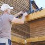 Homme en t-shirt et casquette travaillant sur la toiture en bois d'une (…)