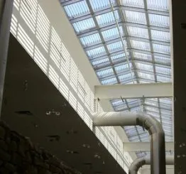 Plafond moderne avec éclairage zénithal, baies vitrées et conduits visibles, créant une ambiance industrielle et lumineuse.