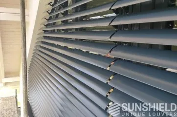 Persiennes en métal gris, disposées parallèlement pour jouer avec la lumière et l’ombre, offrant une touche moderne.