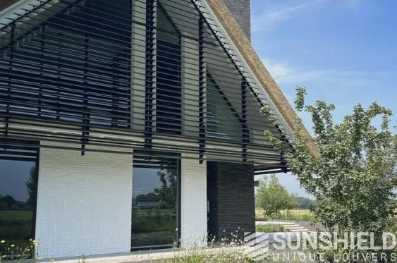 Maison moderne avec façade en briques blanches et noires, toiture inclinée, et store à lamelles. Entourage verdoyant.