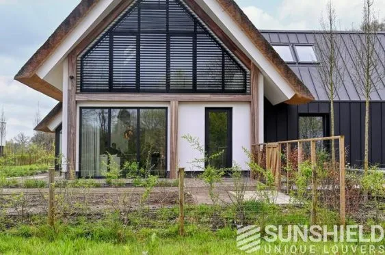 Maison moderne avec façade en bois, grandes fenêtres et toiture en pente, entourée de verdure. Idéale pour un cadre naturel.