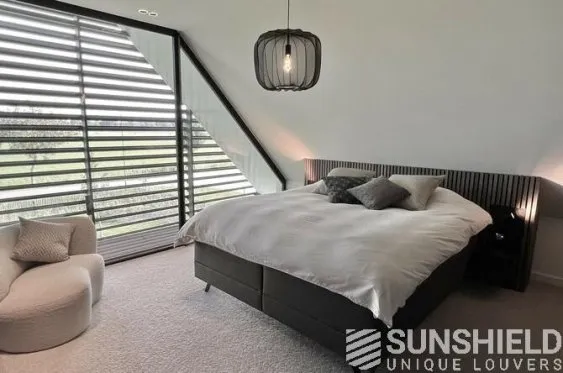 Chambre moderne et lumineuse avec lit élégant, fauteuil confort, grandes fenêtres et stores verticaux. Devise Sunshield.