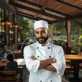 Chef souriant en cuisine extérieure, entouré d’invités dans un restaurant au cadre verdoyant et convivial.