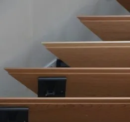 Escalier en bois moderne, avec des marches inclinées et supports métalliques noirs, sur fond de mur neutre.