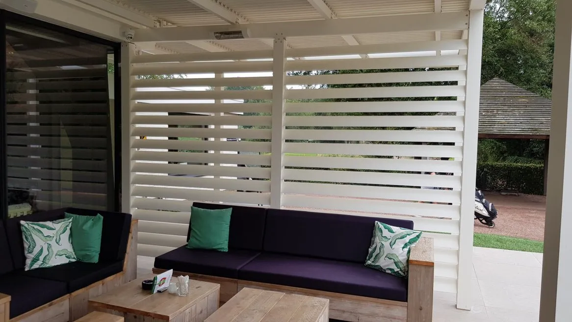 Espace extérieur moderne avec canapés confortables, coussins turquoise et parois en lames blanches pour plus d’intimité.