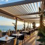 Terrasse moderne avec des tables blanches, chaises noires, et vue sur la mer (…)