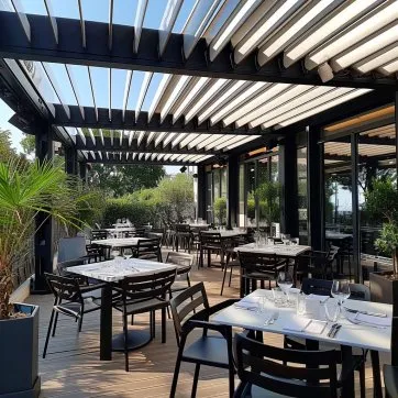 Terrasse de restaurant moderne avec tables élégantes, pergola, verdure et vue sur l’extérieur, idéale pour un repas en plein air.