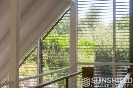 Vue lumineuse à travers des stores à lamelles, offrant une perspective sur un jardin verdoyant, ambiance calme et naturelle.