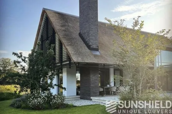 Maison moderne avec toiture en chaume, grandes baies vitrées et jardin verdoyant, offrant une ambiance paisible et naturelle.