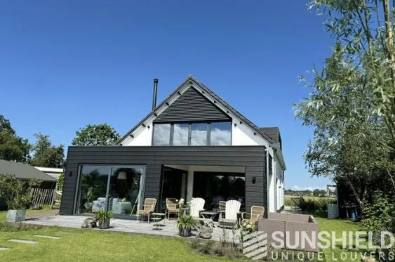 Maison moderne avec façade en bois, terrasse accueillante et jardin verdoyant sous un ciel bleu, parfaite pour la détente.