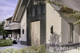 Façade moderne d’une maison avec porte en bois, volets design et jardin verdoyant, créant une ambiance accueillante.