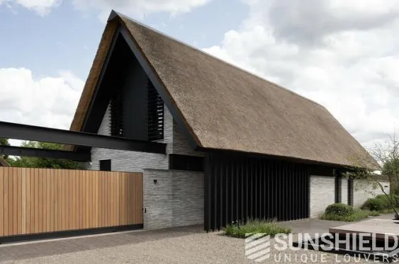 Maison moderne avec toit en chaume, façades noir et gris, intégrée dans un espace paysager minimaliste.