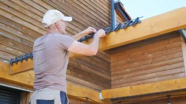Homme en train de fixer des éléments en bois sur une structure extérieure en bois, sous un ciel dégagé.