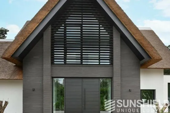 Maison moderne avec toit de chaume, grande baie vitrée et volets en bois, créant une architecture élégante et accueillante.