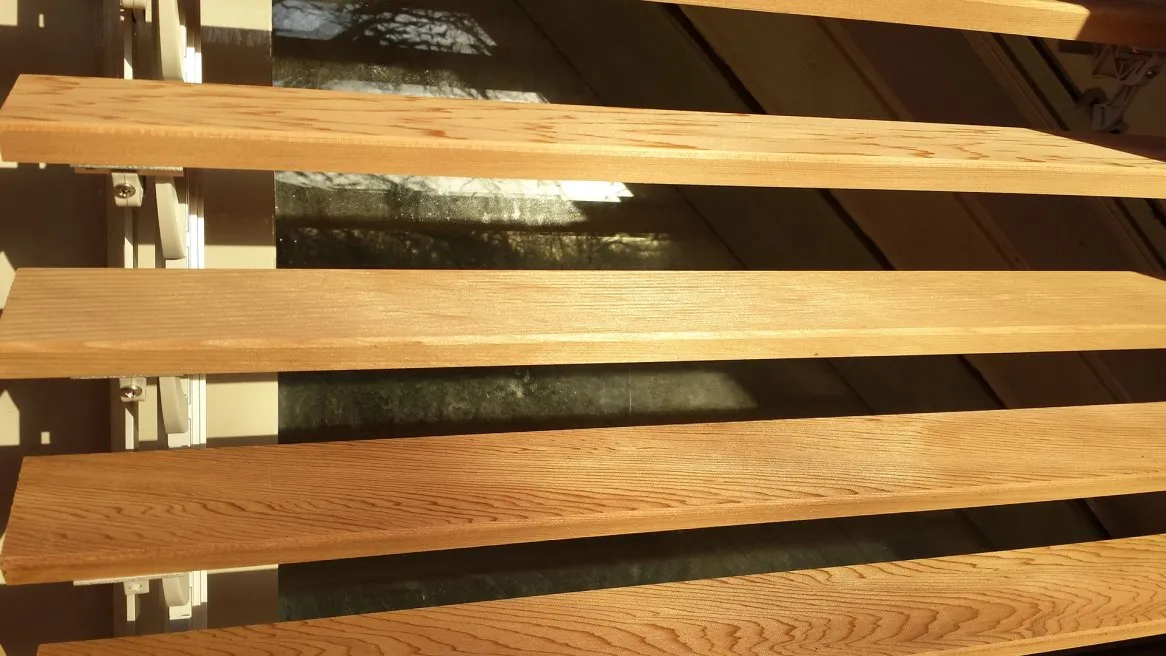 L’image montre des lattes en bois clair disposées horizontalement, filtrant la lumière à travers une fenêtre.