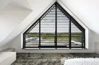 Fenêtre triangulaire avec volets noirs, vue sur un paysage extérieur, pièce moderne avec moquette et mobilier élégant.