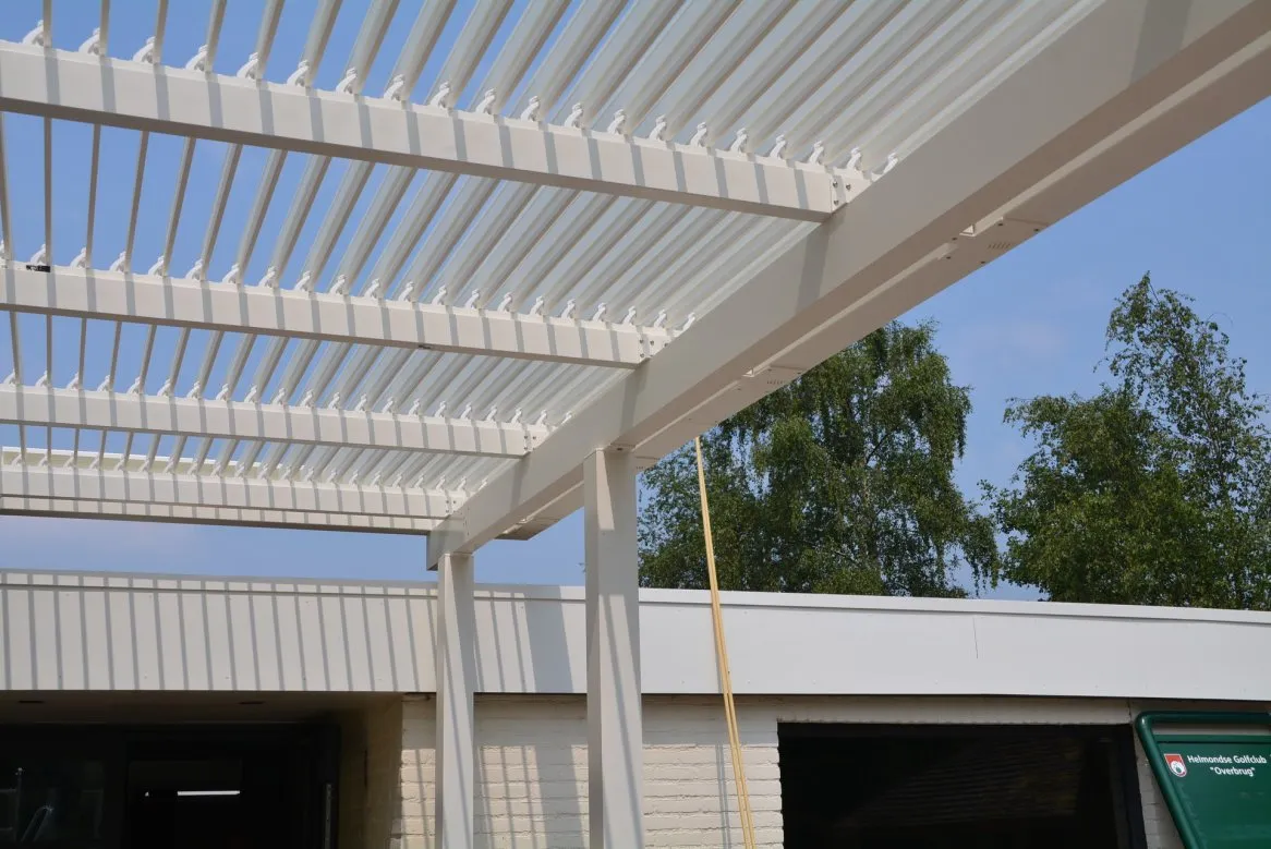 Pergola moderne en aluminium blanc, avec des lattages, sous un ciel bleu dégagé et des arbres en arrière-plan.
