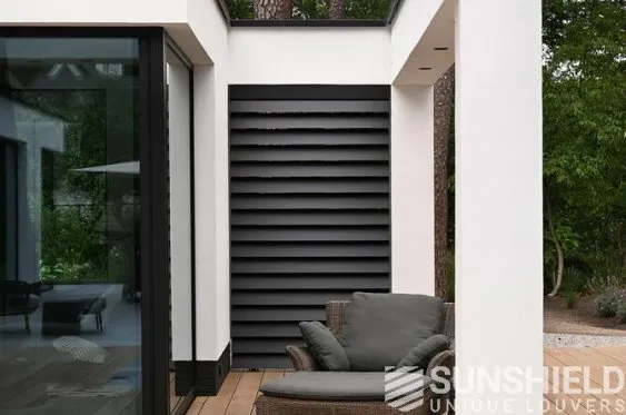 Coin de terrasse moderne avec fauteuil en osier, mur noir à lattes, et végétation luxuriante en arrière-plan.