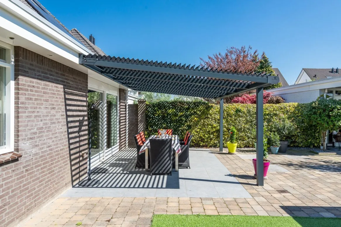 Patio contemporain avec pergola moderne, table en extérieur et chaises colorées, entouré de verdure et beau ciel bleu.